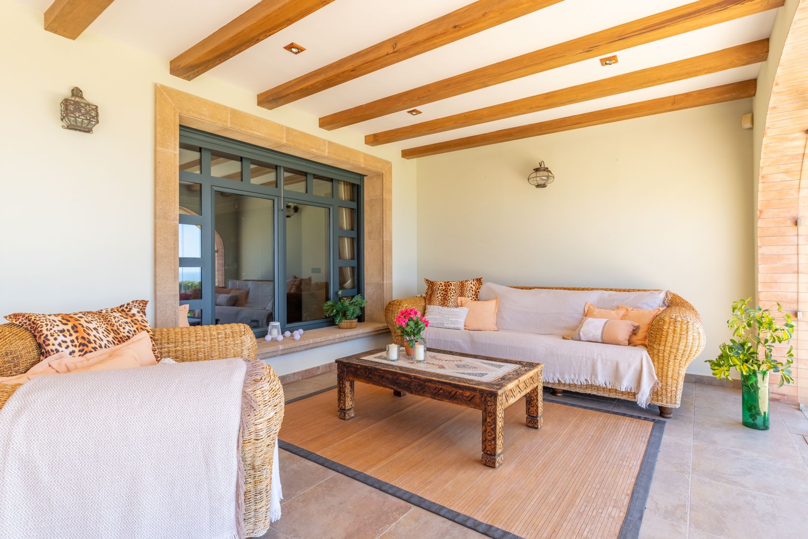 Porche con vigas de madera, sofá y sillón de mimbre, y mesa de centro de madera tallada.