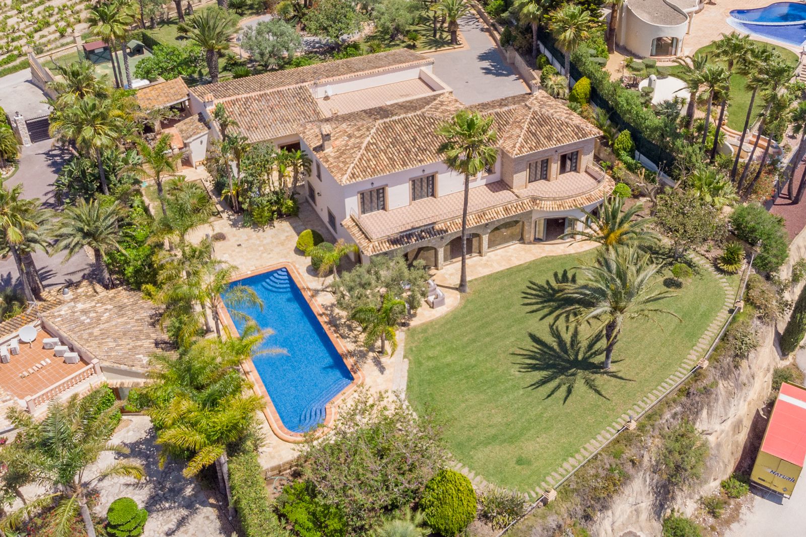 Vista aérea de la finca con piscina azul, jardines maduros y arquitectura mediterránea.