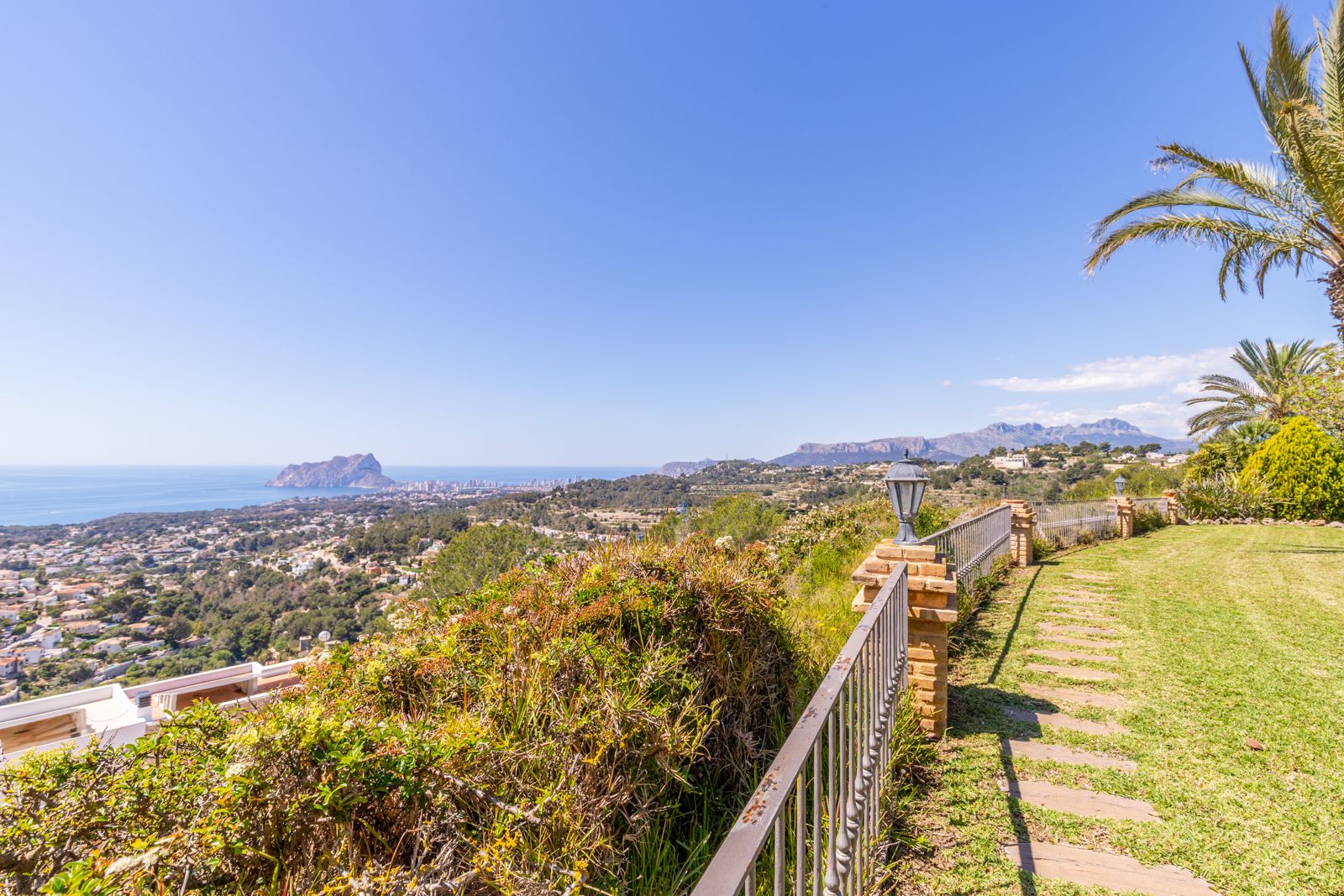 Vista panorámica desde el jardín con camino empedrado y barandilla metálica.