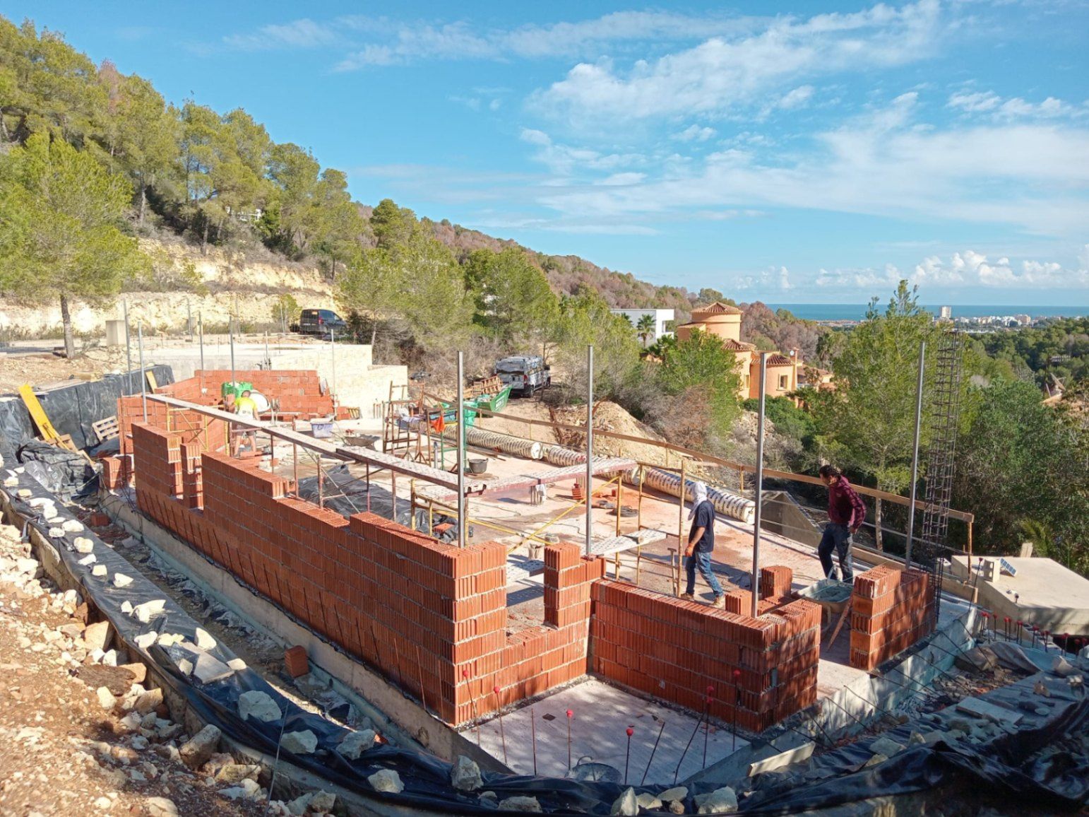 Fase inicial de construcción de la villa en Jávea, mostrando el levantamiento de muros con bloque cerámico sobre la cimentación y vistas panorámicas al mar Mediterráneo.
