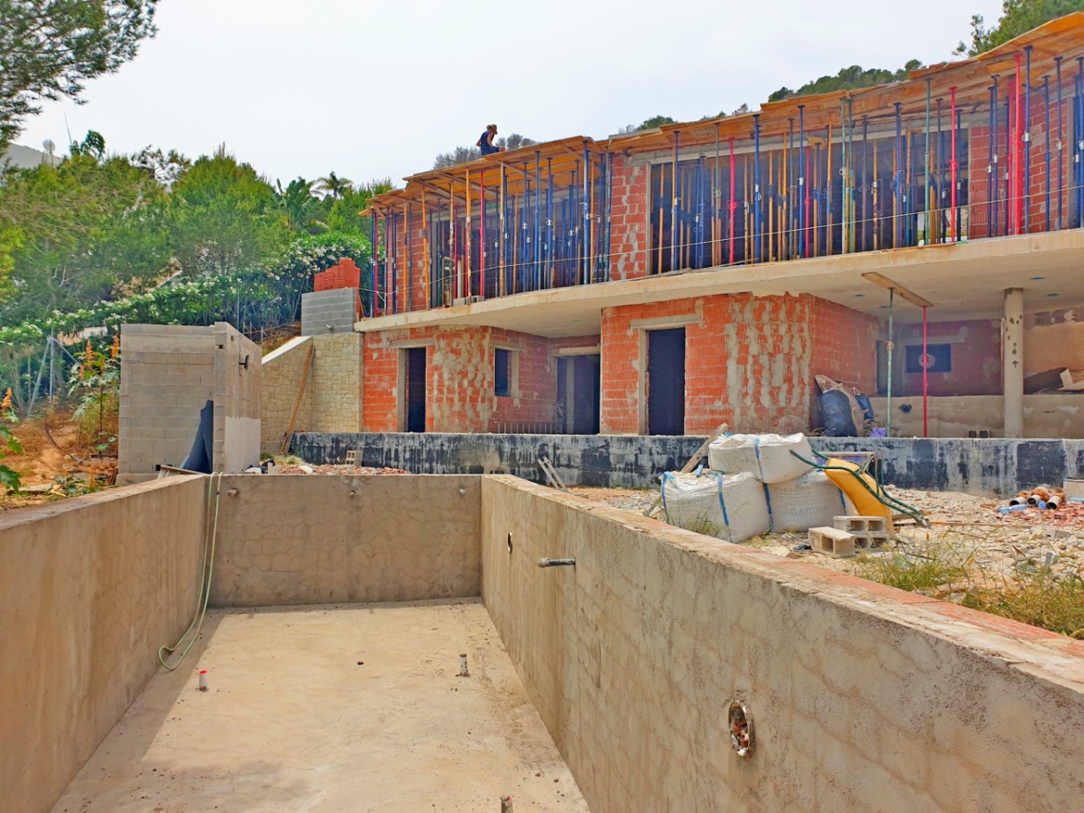 Vista del estado actual de construcción con la estructura de ladrillo, puntales metálicos y el vaso de hormigón de la piscina en primer plano.