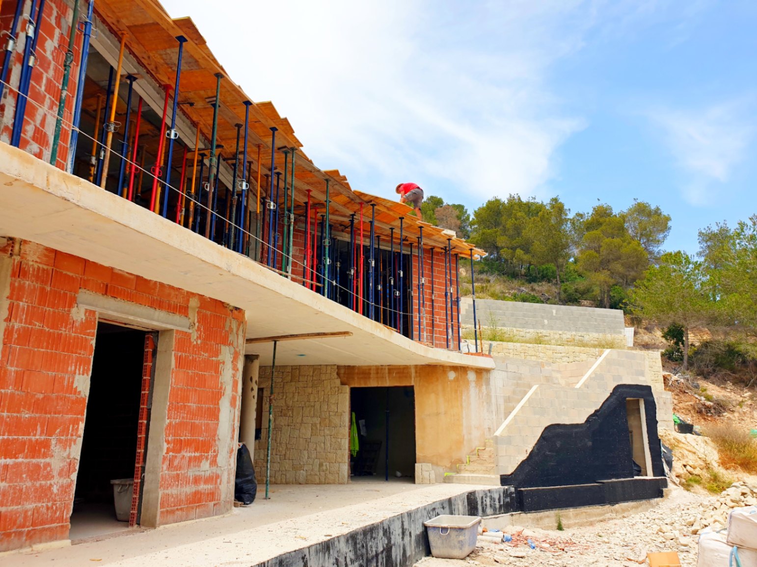Vista exterior de la estructura en construcción, destacando la fachada de ladrillo, muros de piedra natural y el forjado curvo de la terraza.