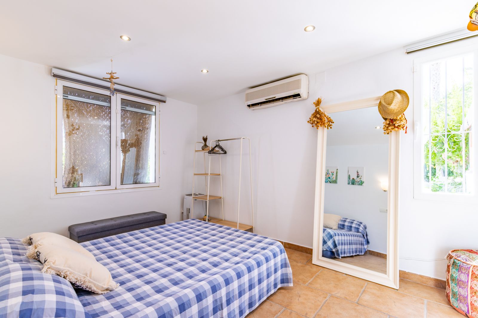 Dormitorio luminoso con suelos de terracota, aire acondicionado y un gran espejo de pie. La estancia cuenta con iluminación empotrada y acceso a luz natural.
