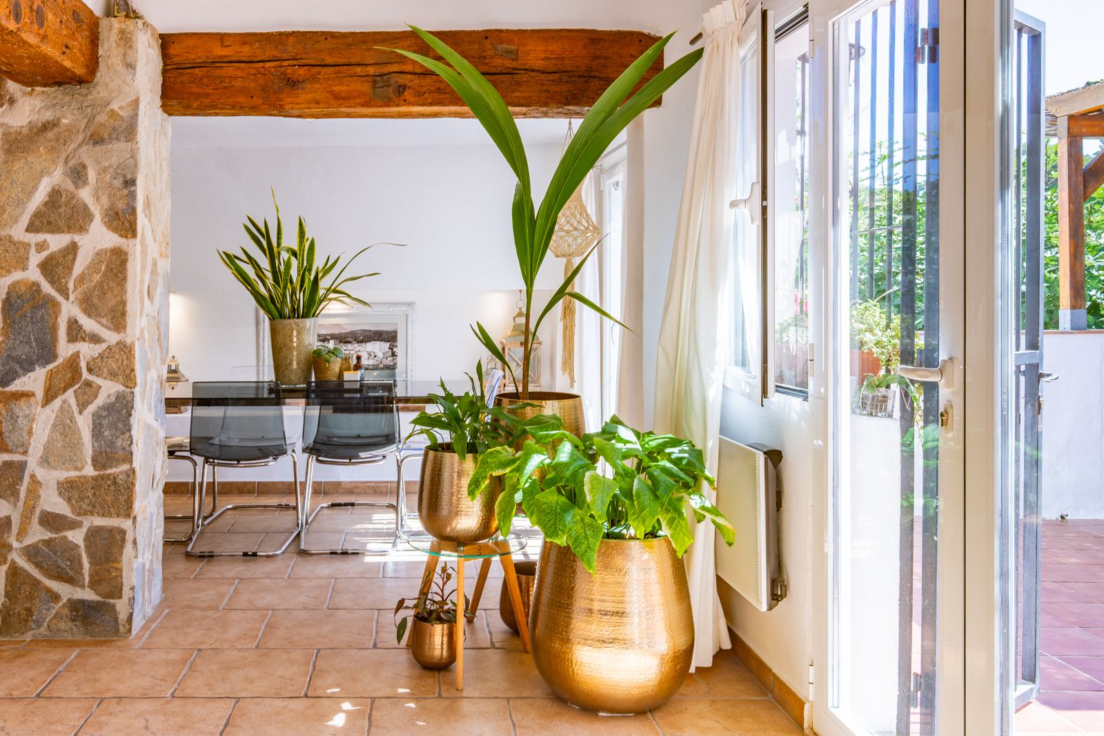 Salón comedor con vigas de madera vista, pilar de piedra natural y suelos cerámicos. Los grandes ventanales integran el interior con la luz natural del exterior.