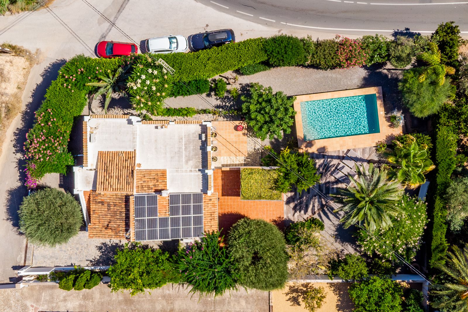 Vista aérea cenital que muestra la distribución de la parcela, destacando la piscina privada, el sistema de placas solares en el tejado y el frondoso jardín mediterráneo.