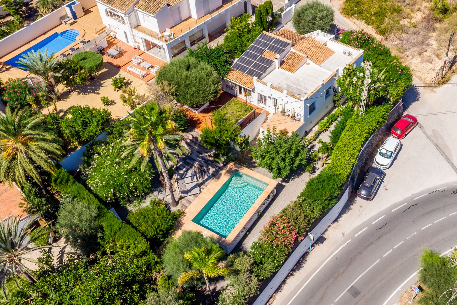 Vista aérea de la villa destacando la piscina rectangular, el jardín mediterráneo maduro y la instalación de placas solares sobre el tejado de teja.