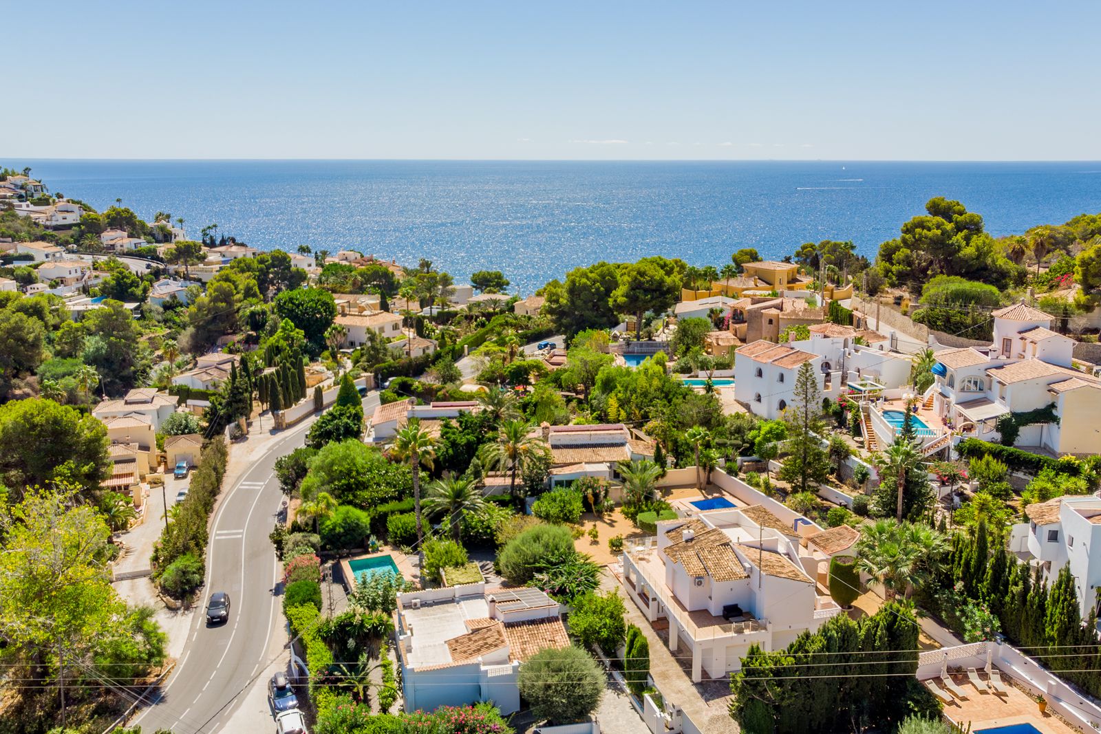 Vista aérea panorámica de la zona costera de Baladrar, destacando la proximidad al mar Mediterráneo y el entorno arbolado salpicado de villas blancas.