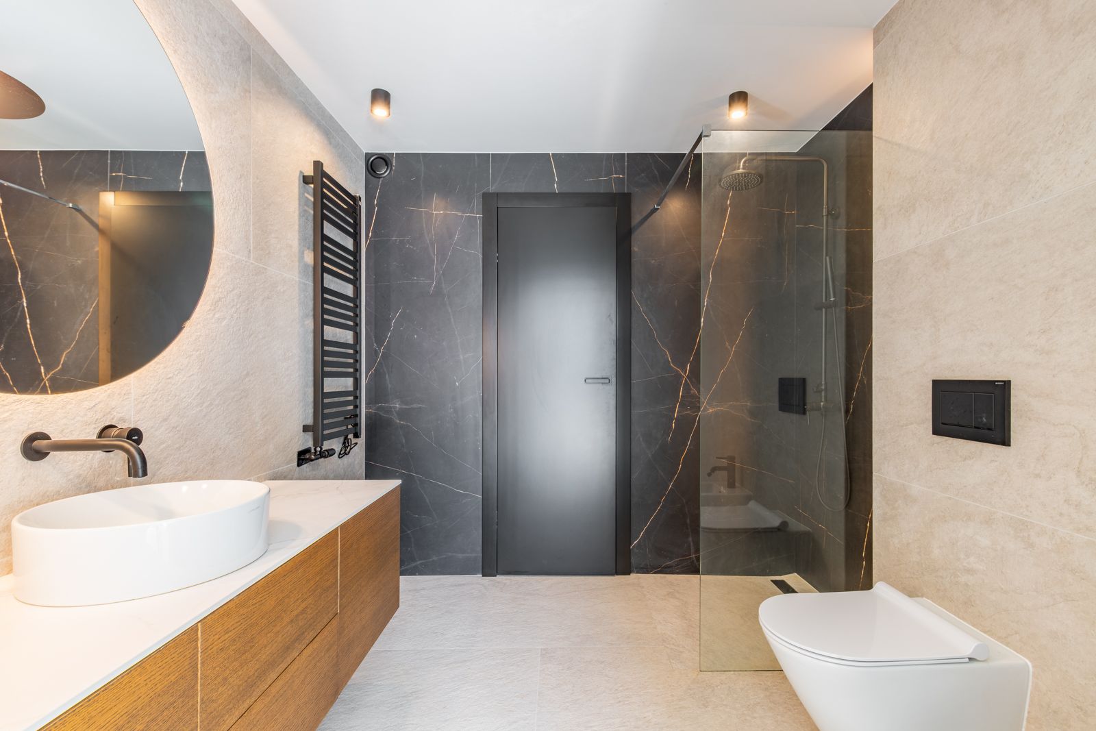 Baño de diseño con gres porcelánico de gran formato, espejo retroiluminado, lavabo sobre encimera de madera y ducha con mampara de cristal y grifería negra mate.