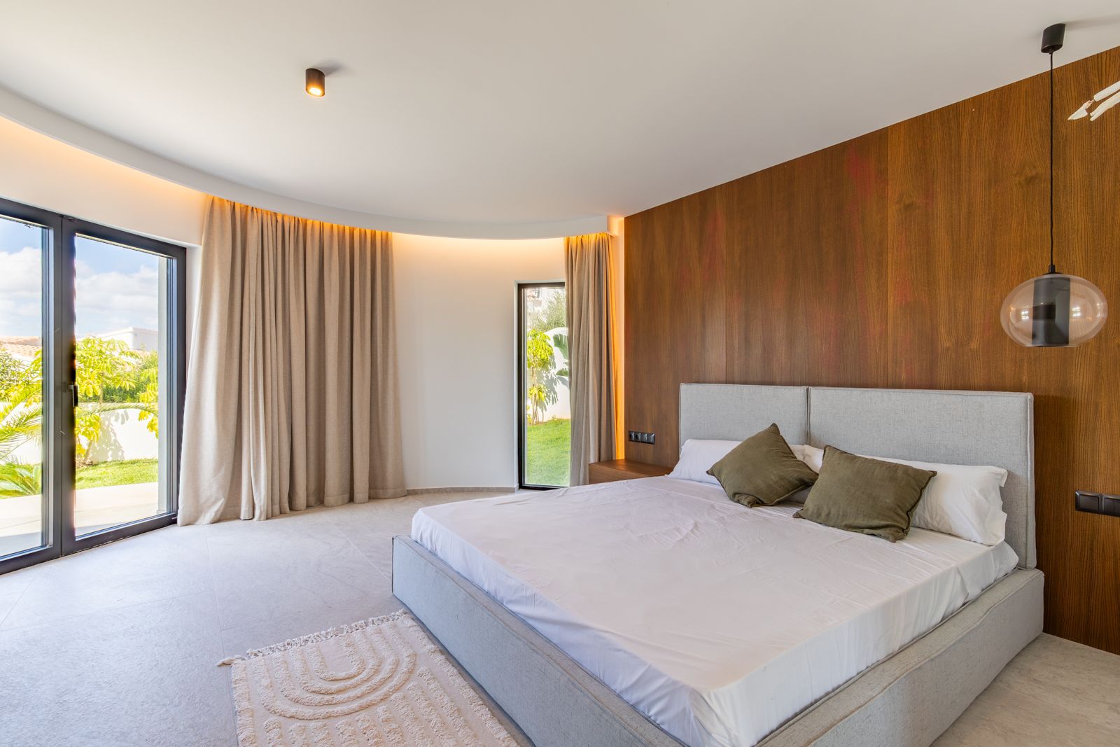 Dormitorio principal con panelado de roble natural, iluminación LED indirecta en techo curvo y acceso directo al jardín mediante ventanales de gran formato.
