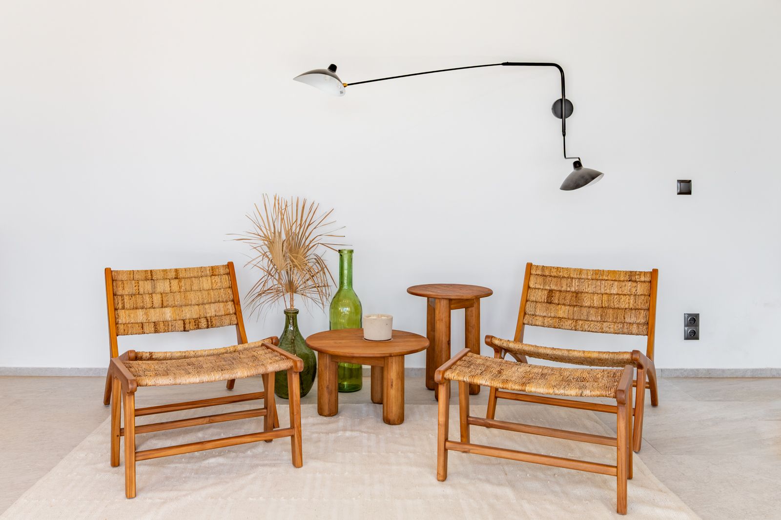 Rincón de lectura con butacas de madera y fibra natural, mesas de teca y aplique de diseño articulado en negro sobre suelo de gres porcelánico.