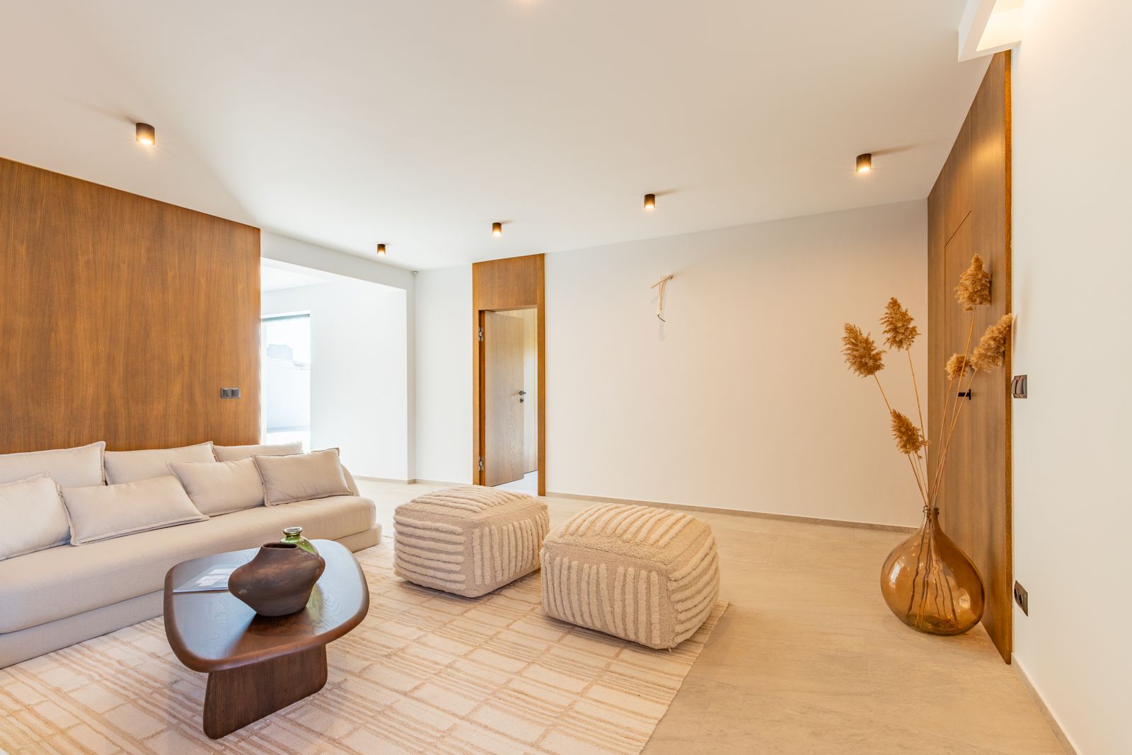 Salón minimalista con revestimiento de pared en roble natural, suelos de gres porcelánico de gran formato y mobiliario de diseño iluminado por focos empotrados.