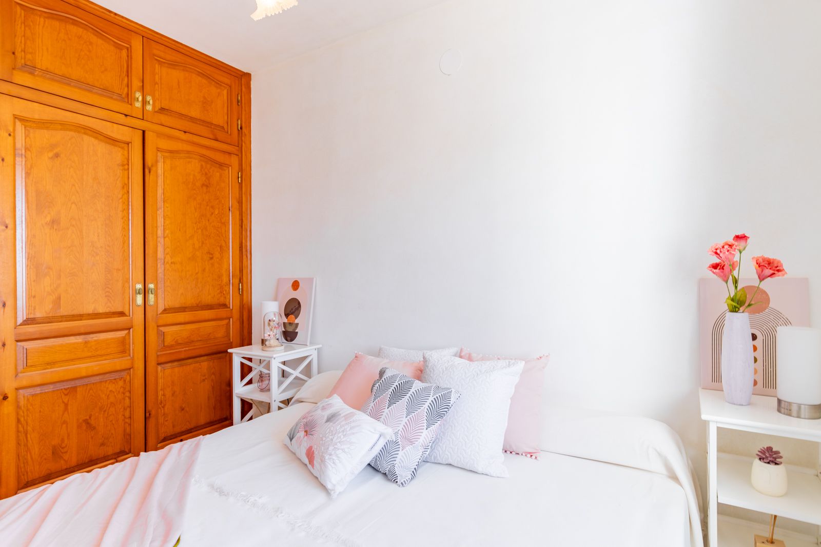 Dormitorio luminoso con un gran armario empotrado de madera de estilo tradicional, paredes blancas y mesitas auxiliares que aportan funcionalidad y calidez.