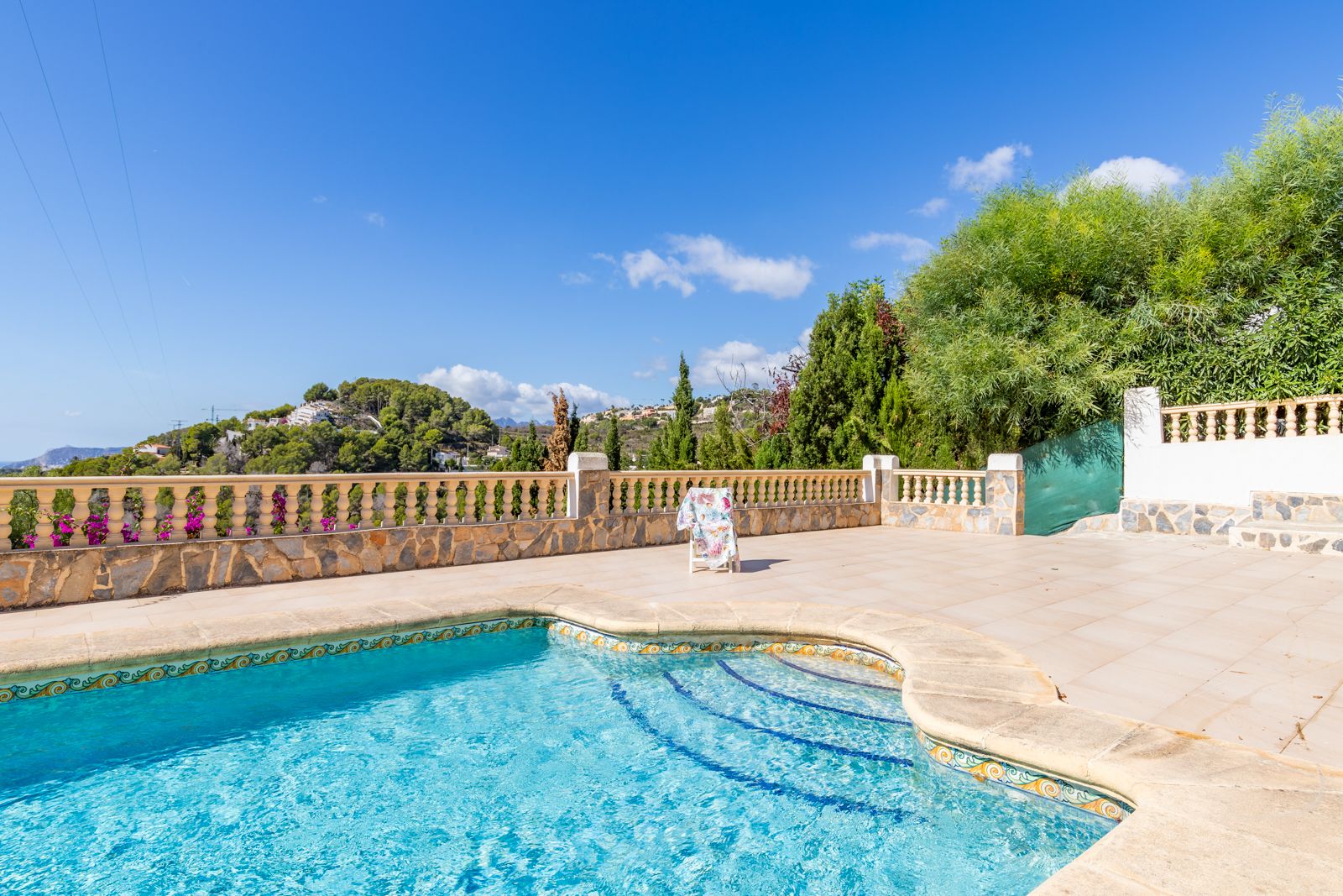 Piscina privada con borde cerámico decorativo y amplia terraza de baldosas, rodeada por una balaustrada de piedra natural con vistas despejadas a las colinas.