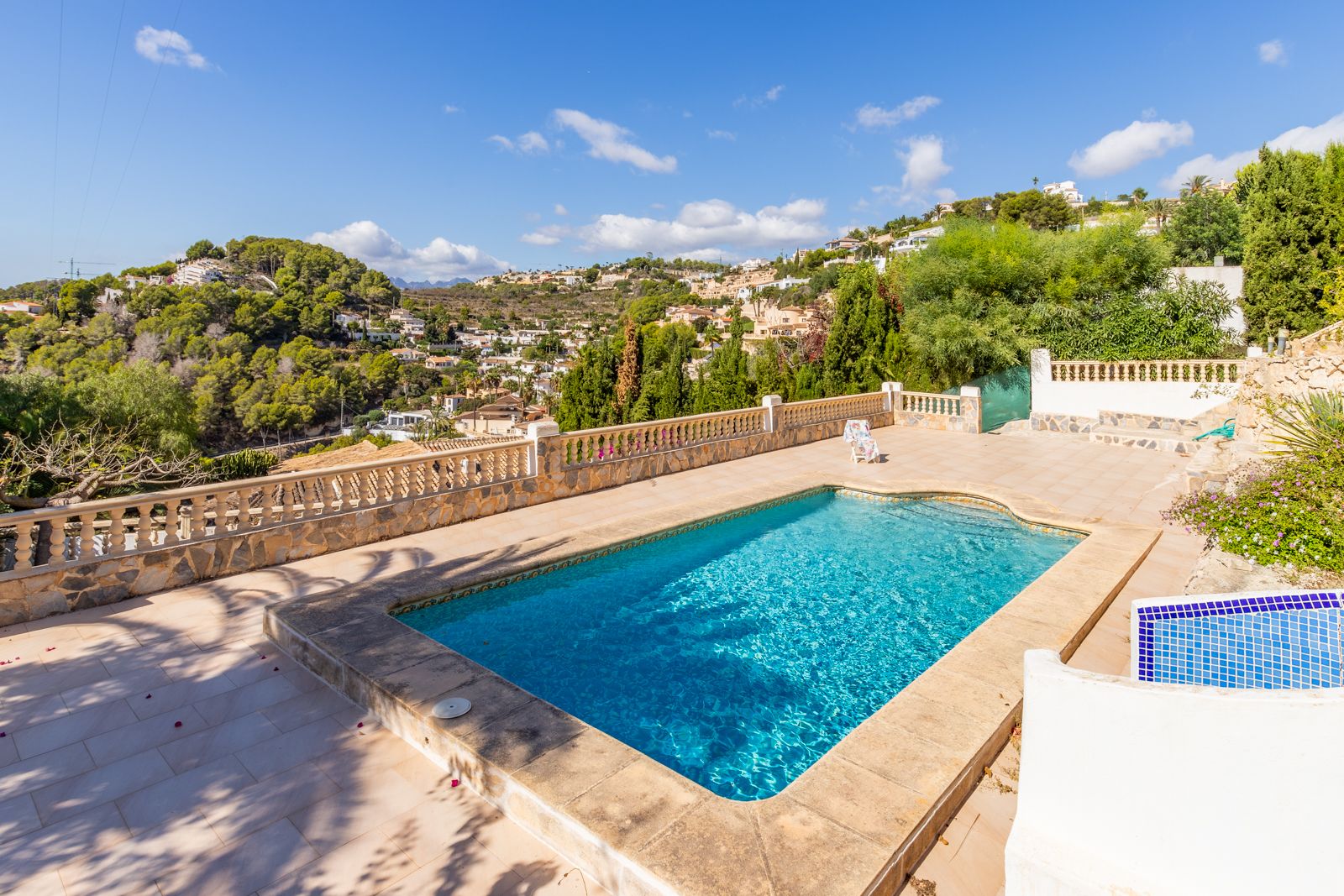 Piscina privada rectangular rodeada de una amplia terraza de piedra, con balaustrada clásica y vistas despejadas a las colinas arboladas de Benimeit.