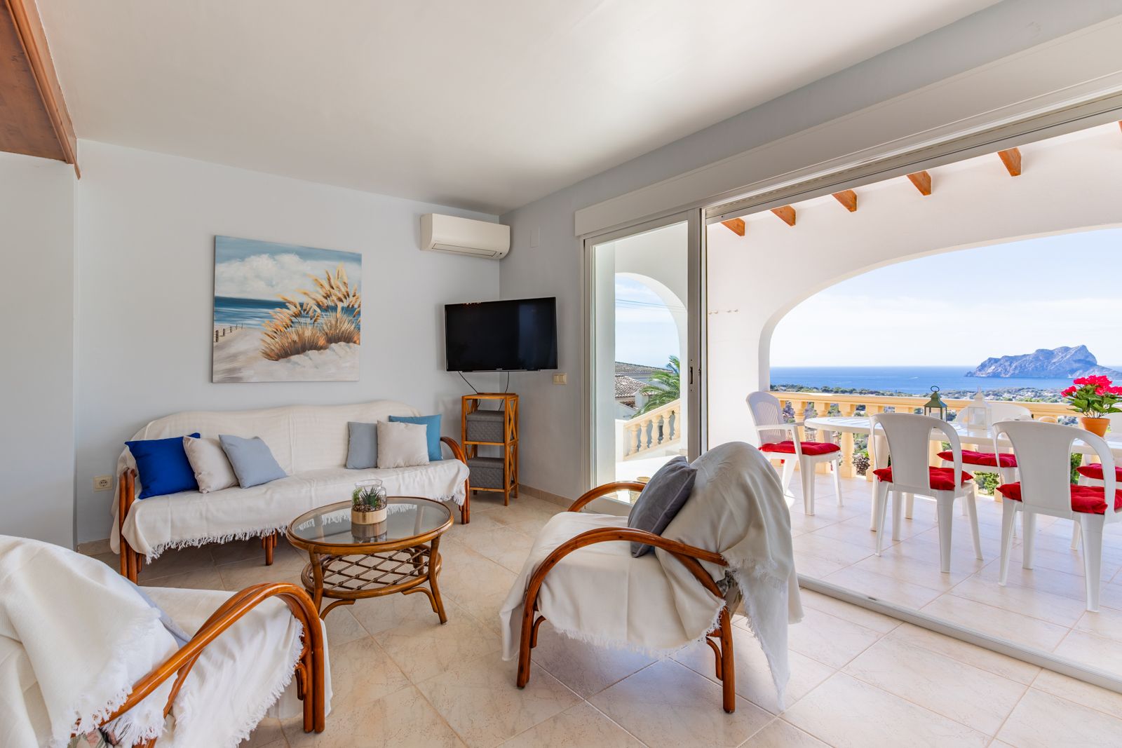 Salón luminoso con muebles de bambú y acceso directo a una naya arqueada. Ofrece vistas panorámicas al mar Mediterráneo y al Peñón de Ifach desde la terraza.