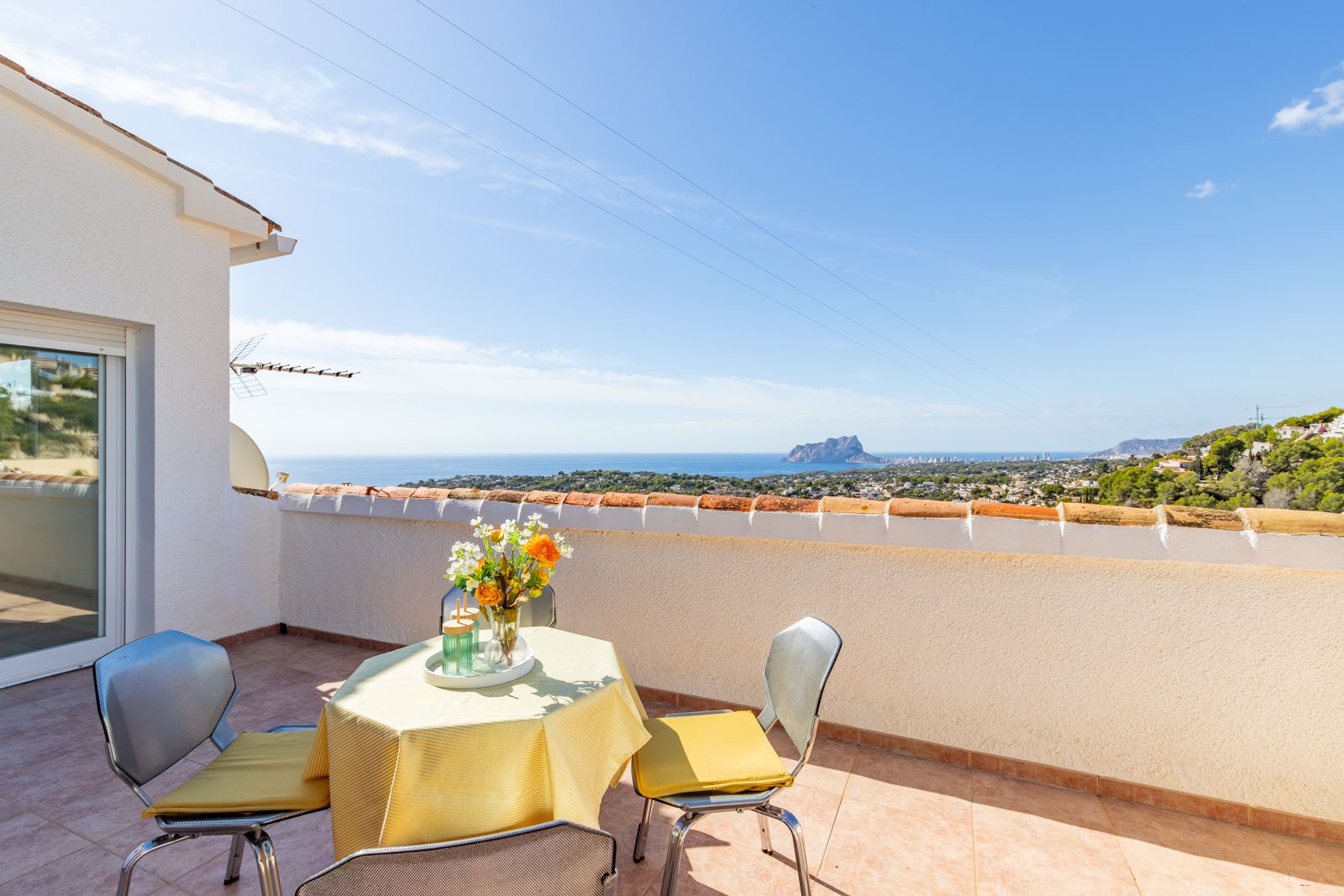 Terraza elevada con suelos cerámicos y vistas panorámicas al mar Mediterráneo y al Peñón de Ifach, equipada con una zona de estar exterior bajo el sol.