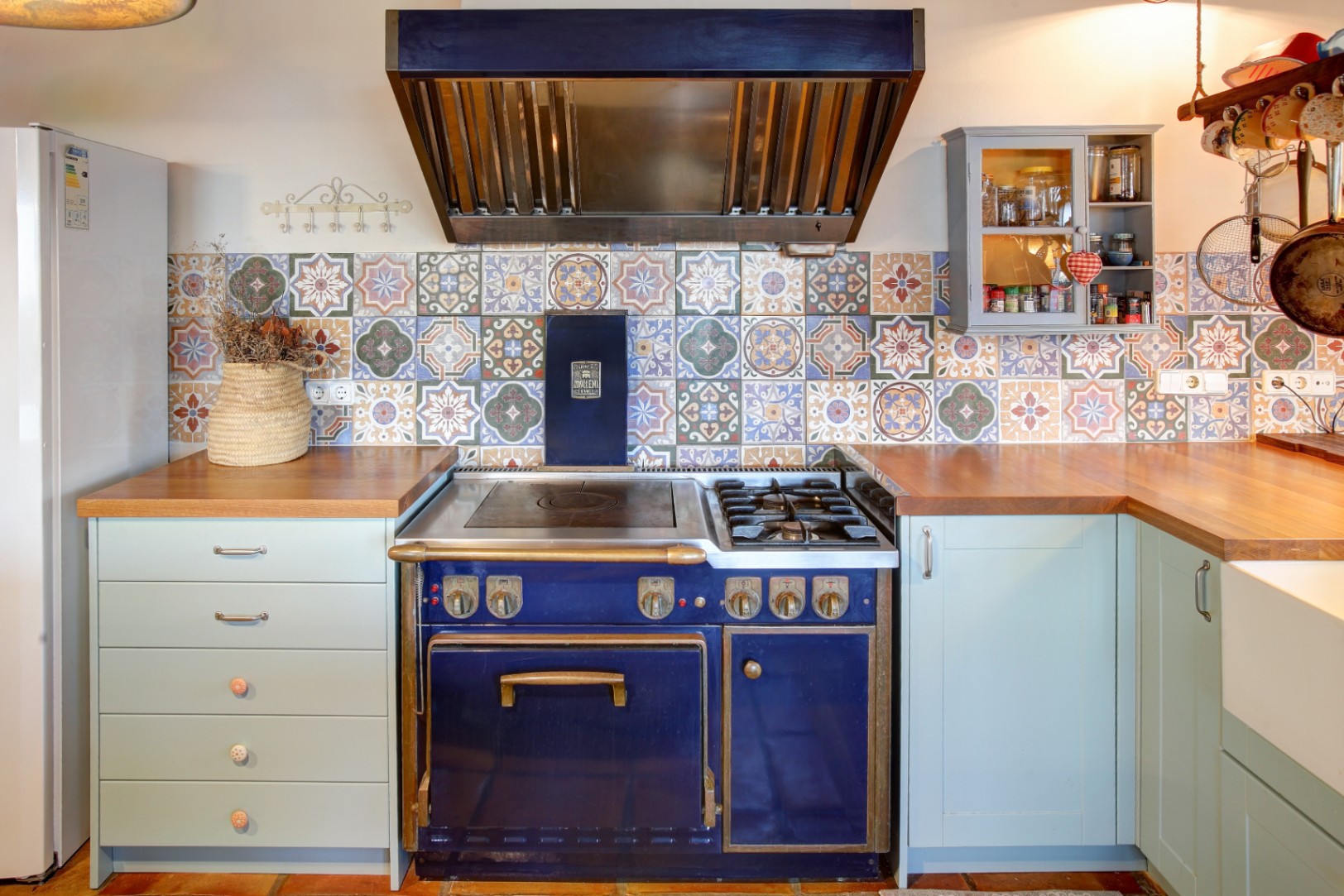 Cocina profesional Molteni en azul cobalto con detalles en latón, integrada entre encimeras de madera natural y un frontal de azulejos hidráulicos con motivos geométricos.