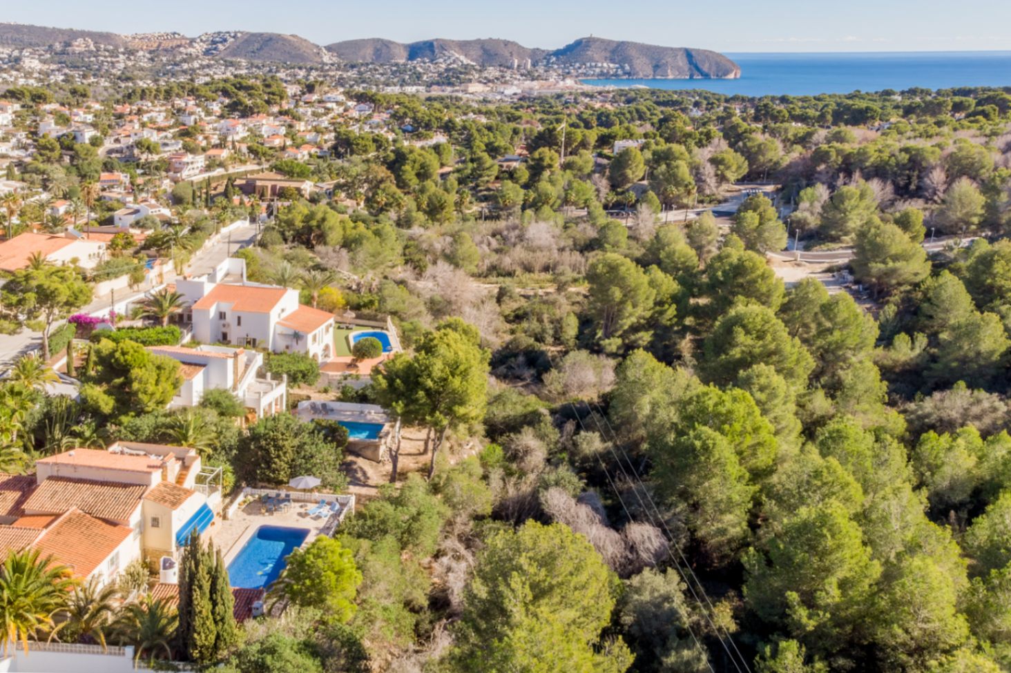 Vista aérea que destaca la ubicación privilegiada junto a una zona verde protegida, con vistas panorámicas al mar Mediterráneo y la costa de Moraira.