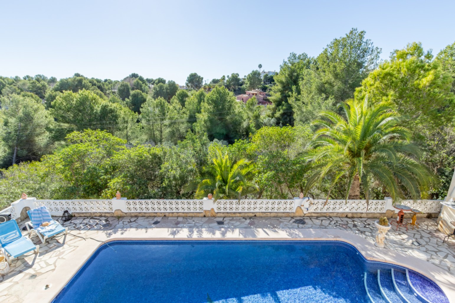 Vista elevada de la piscina de 42 m² y terraza de piedra natural, rodeada por una balaustrada blanca y vistas directas a la zona verde protegida de Moraira.