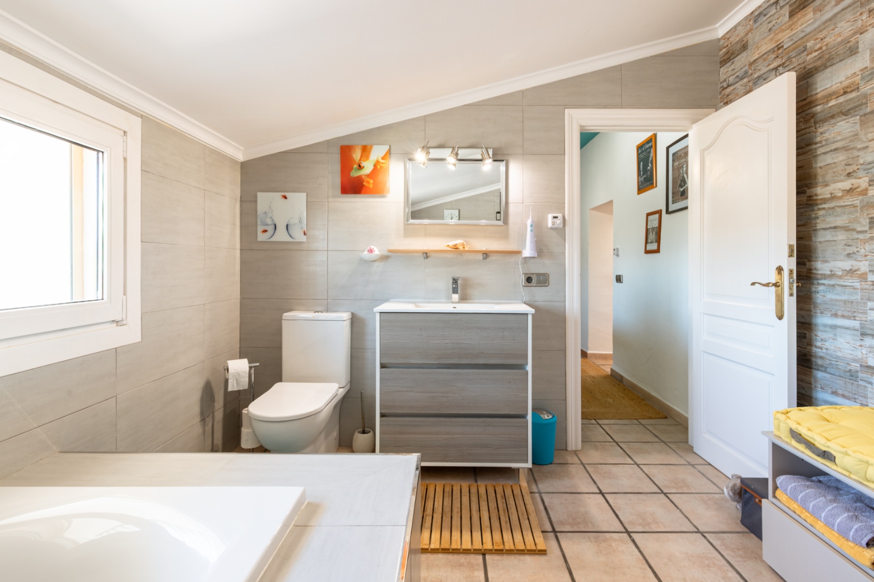 Cuarto de baño reformado con techo inclinado, mueble de lavabo en acabado madera y paredes revestidas en gres porcelánico de gran formato.