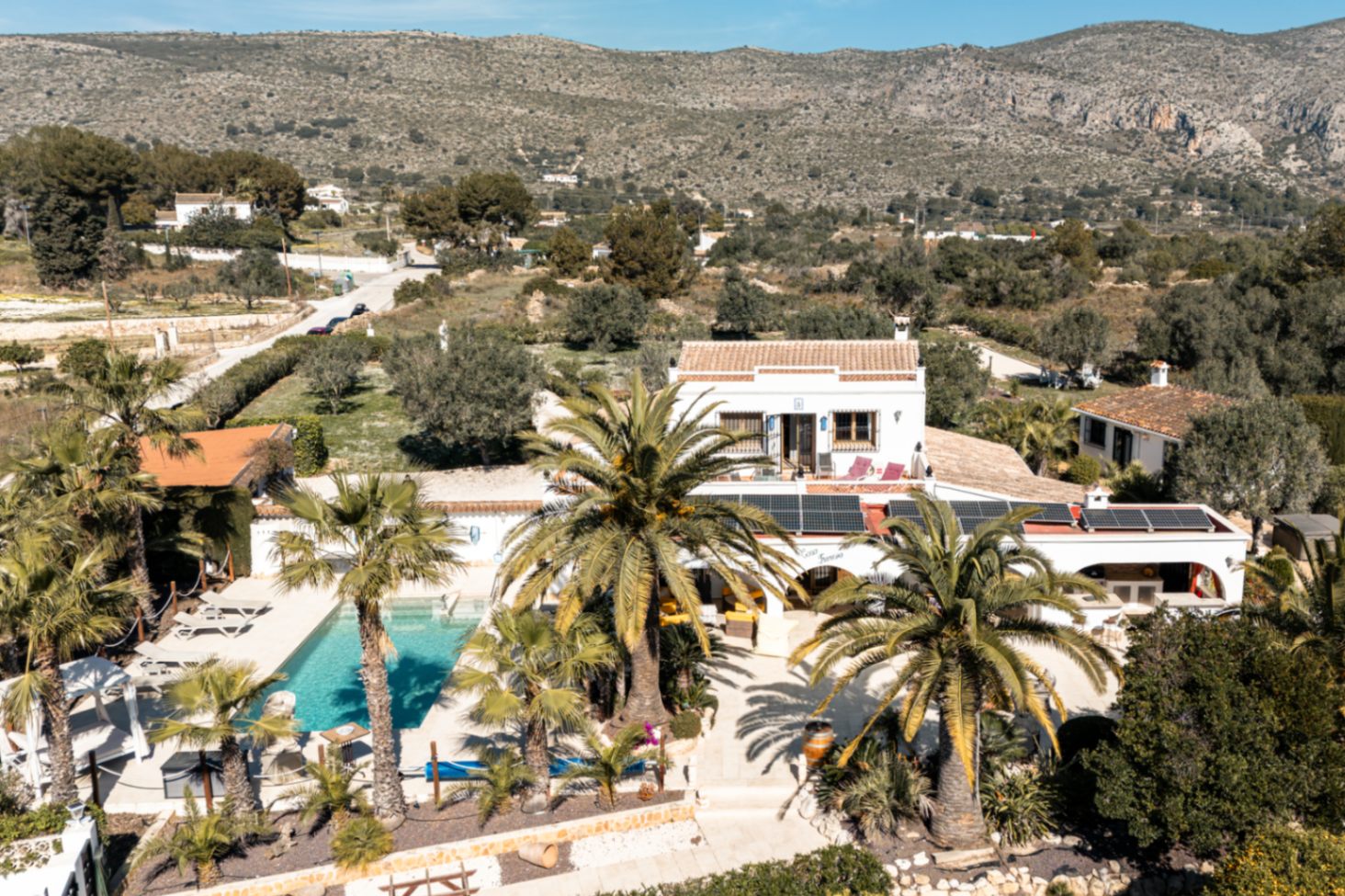 Vista aérea de la finca destacando la piscina, la instalación de paneles solares y el entorno natural con palmeras y vistas a las montañas.