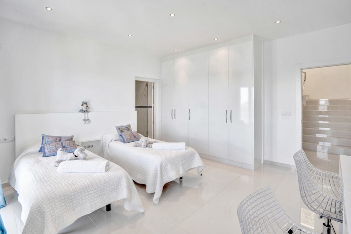 Dormitorio doble de diseño minimalista con armarios empotrados de alto brillo, suelos cerámicos blancos y acceso directo a baño en suite.