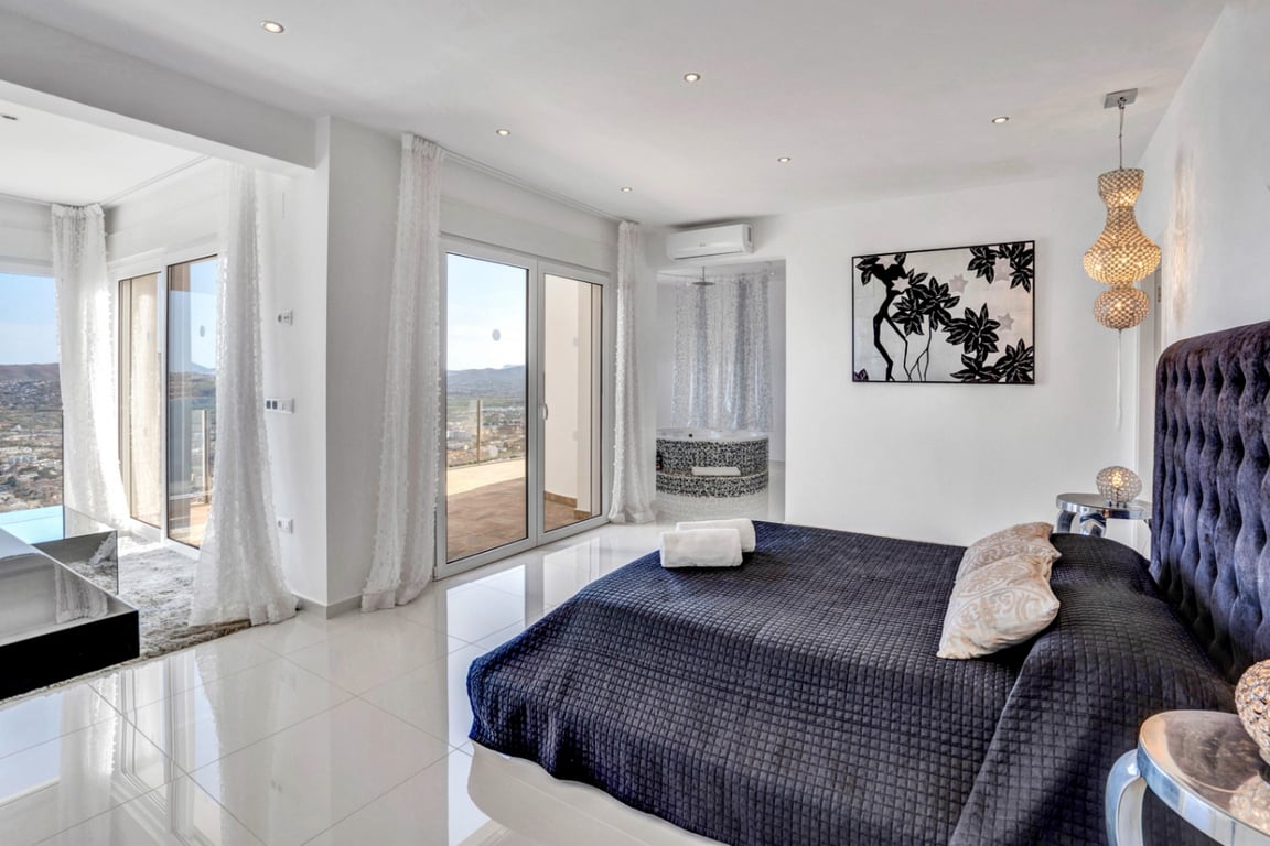 Dormitorio principal con cama de diseño, cabecero capitoné y acceso directo a la terraza. Incluye un jacuzzi integrado con mosaicos y vistas panorámicas al Mediterráneo.