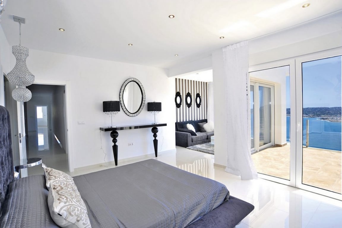 Dormitorio principal con suelos de gres blanco, zona de estar integrada y acceso directo a una terraza con vistas panorámicas al mar Mediterráneo.