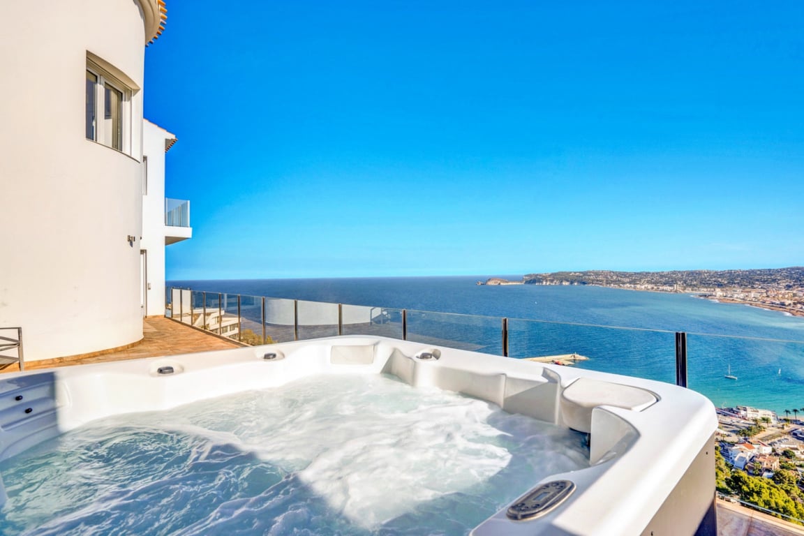 Jacuzzi exterior en terraza elevada con barandilla de cristal, ofreciendo vistas panorámicas al mar Mediterráneo y al puerto de Jávea.