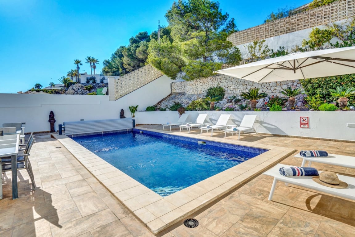 Piscina exterior privada rodeada de una terraza de gres, zona de solárium con hamacas blancas y muros de piedra natural integrados en el paisaje.