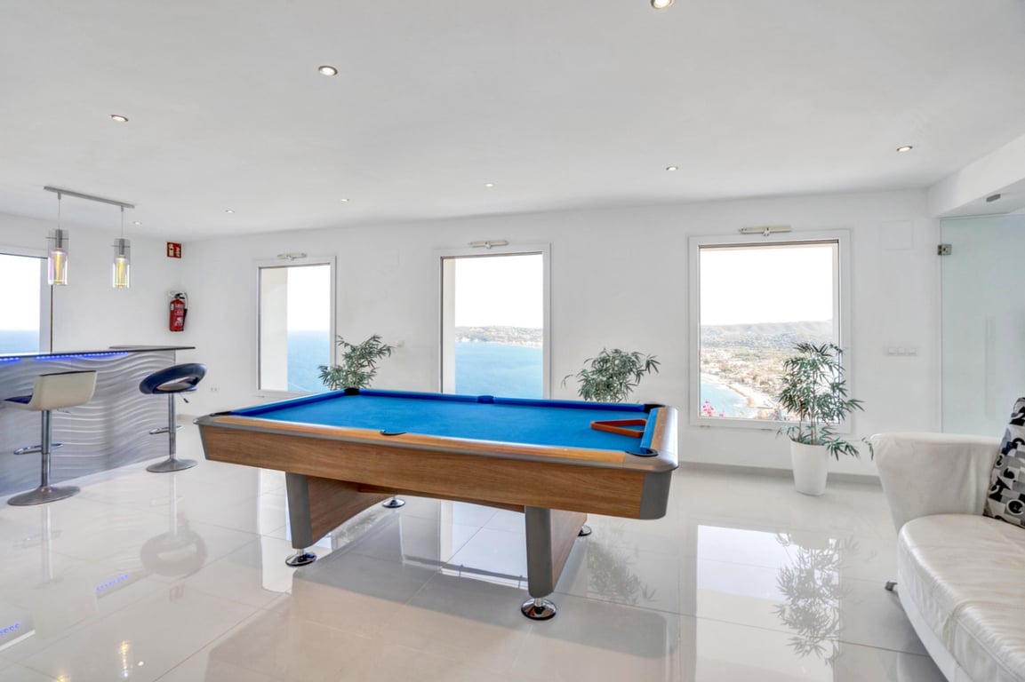 Sala de juegos con mesa de billar, zona de bar integrada y amplios ventanales con vistas panorámicas al mar Mediterráneo y la costa de Jávea.