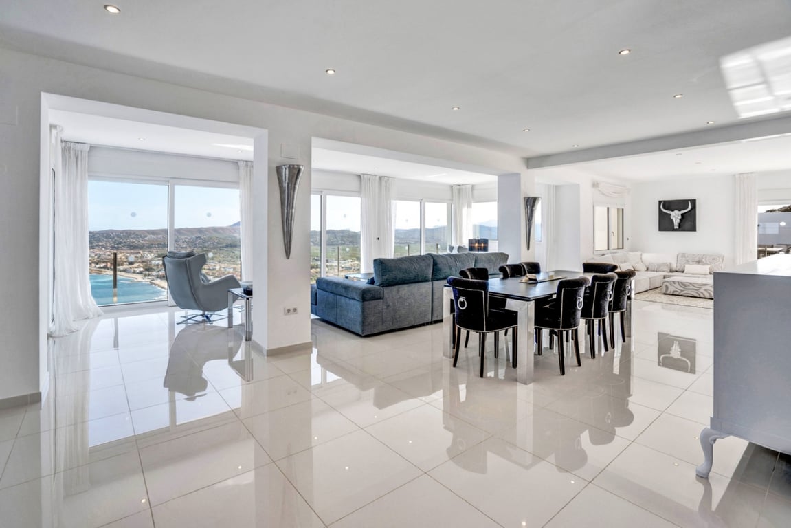 Salón-comedor diáfano con suelos porcelánicos de alto brillo y amplios ventanales que ofrecen vistas panorámicas a la bahía de Jávea y el entorno montañoso.