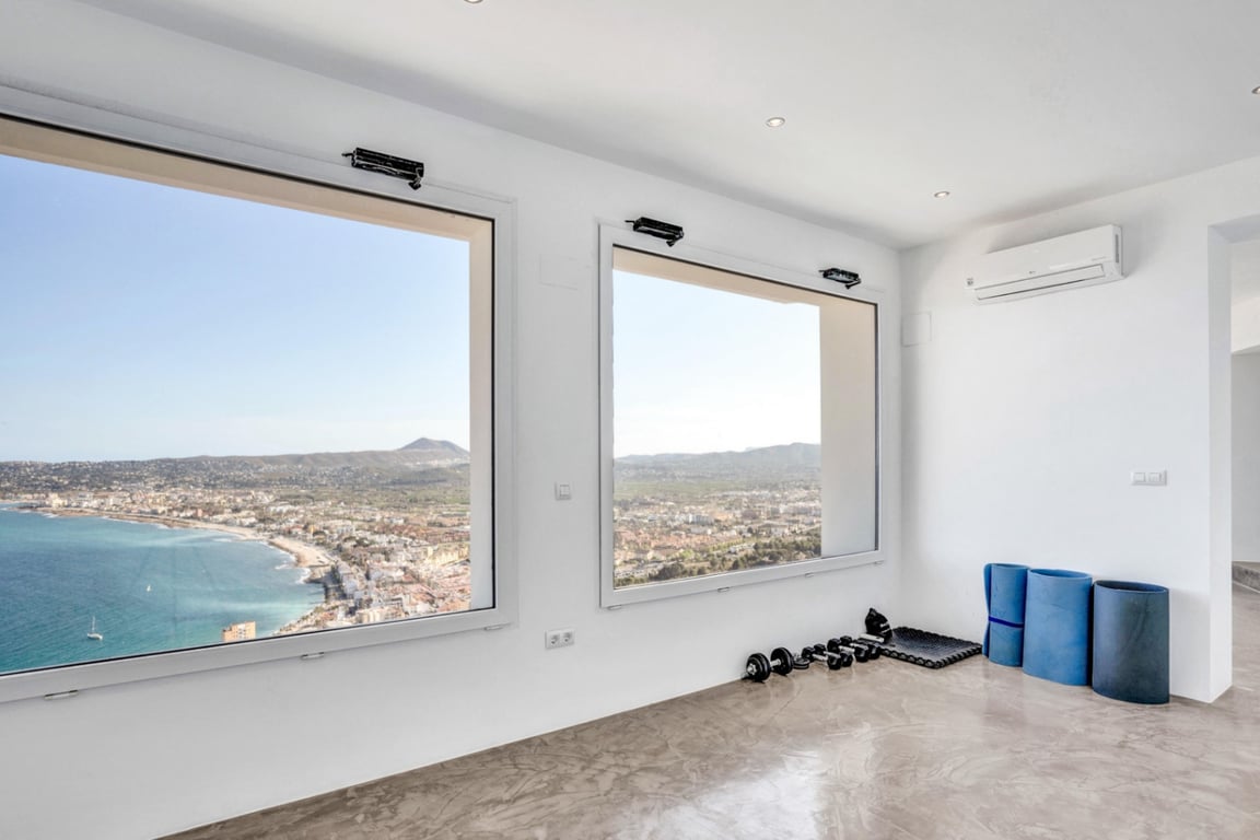 Zona de yoga y fitness con suelo de microcemento y grandes ventanales que ofrecen vistas panorámicas a la bahía de Jávea y al mar Mediterráneo.