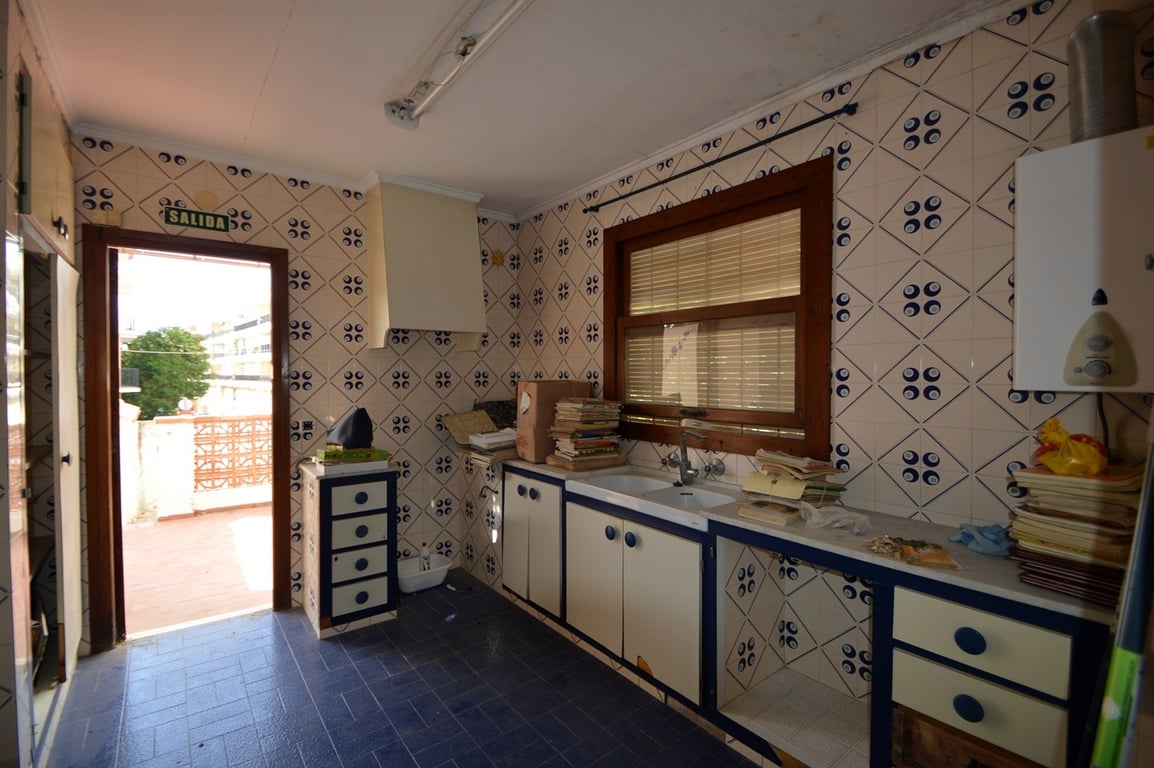 Cocina con azulejos decorativos, suelos azules y acceso directo a la terraza. Incluye un fregadero doble, ventana de madera y armarios con perfiles en azul.