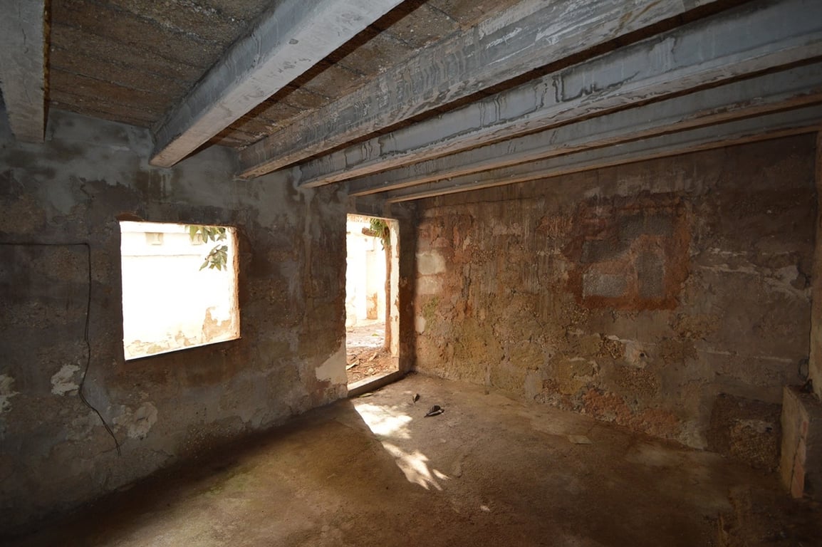Espacio diáfano en bruto con paredes de piedra original y vigas de hormigón a la vista. Cuenta con luz natural y acceso directo al patio exterior para reformar.