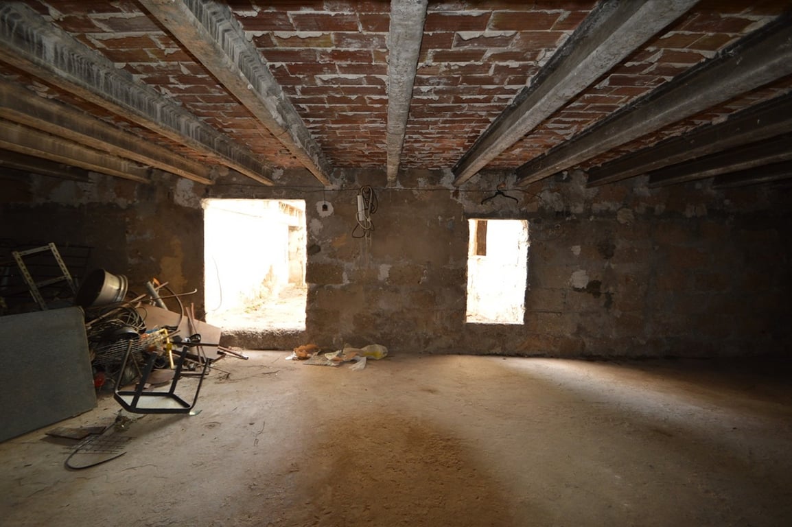 Espacioso interior diáfano para reformar con techos de vigas de hormigón y bovedilla de ladrillo visto. La estancia cuenta con muros de piedra natural y dos aberturas al exterior.