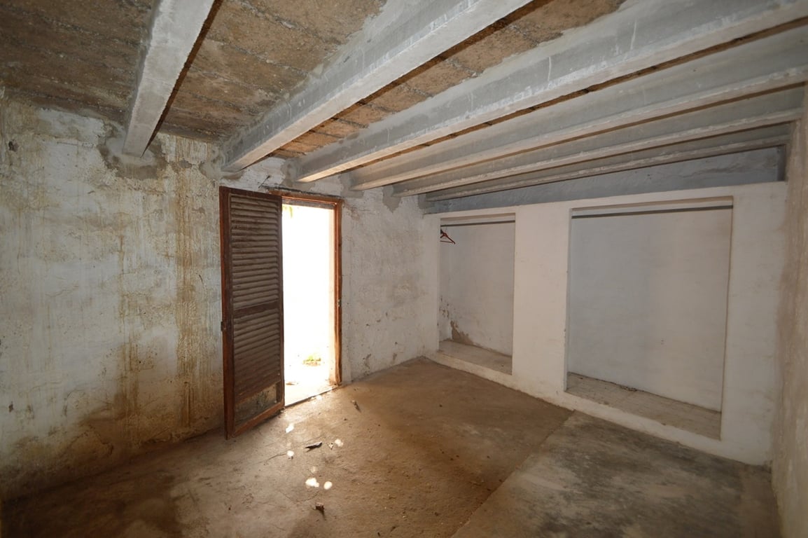Espacioso trastero con vigas de hormigón a la vista, nichos de almacenamiento integrados y acceso directo al exterior mediante una puerta de madera mallorquina.