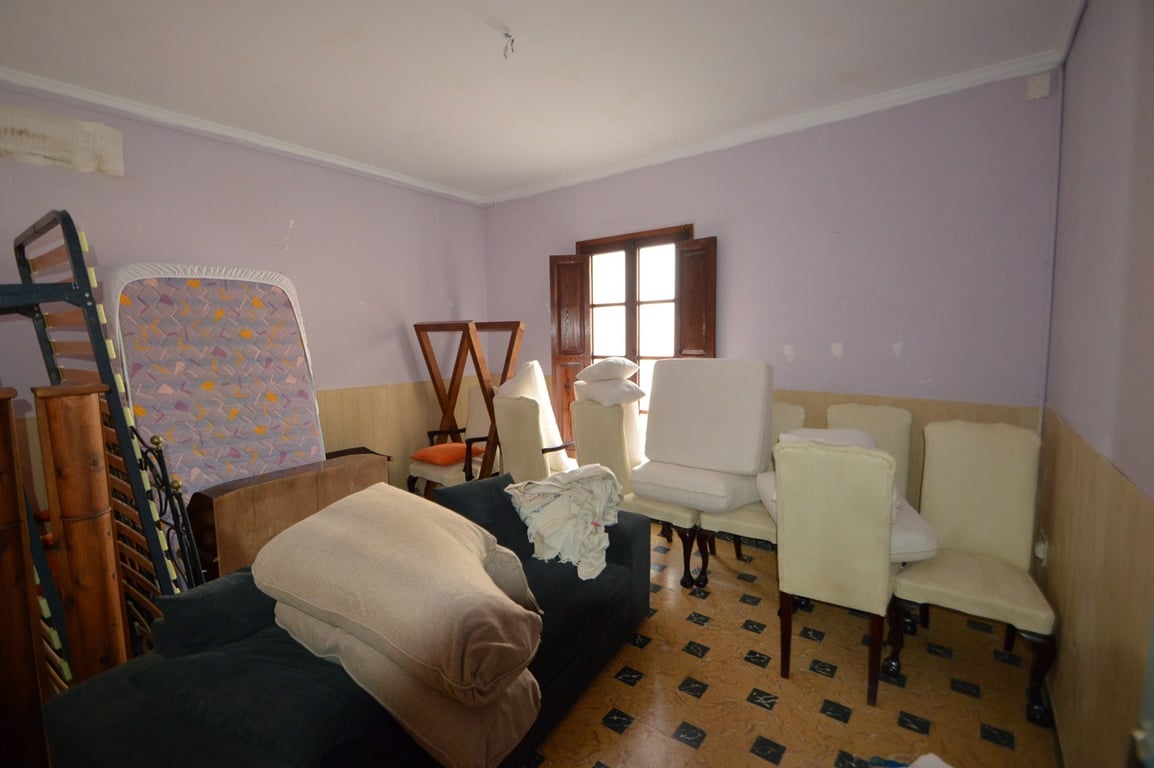 Habitación amplia con paredes en tono lavanda y zócalo de madera, suelos de baldosa con diseño y ventana tradicional de madera con contraventanas.