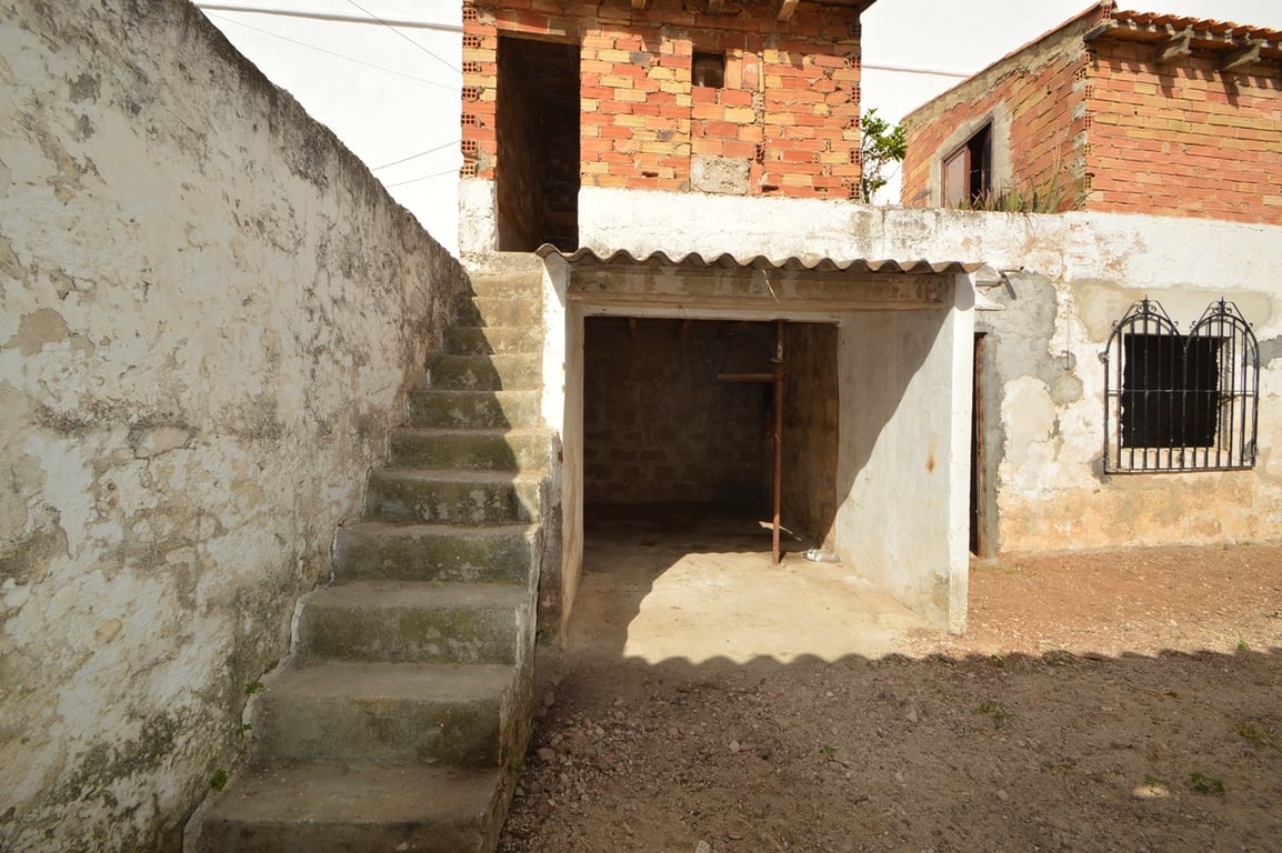 Patio exterior con escaleras de hormigón, zona de almacenamiento cubierta y muros de ladrillo visto listos para reformar en el casco antiguo.