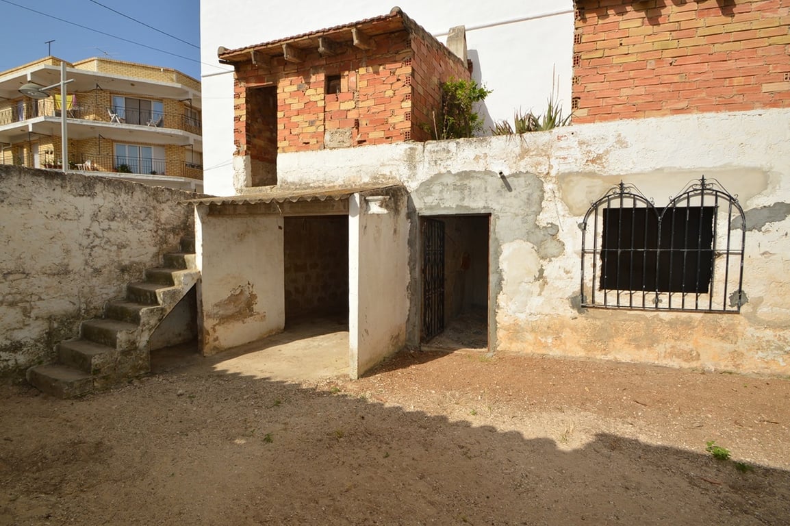 Patio interior con muros de ladrillo visto, escalera de piedra y dependencias anexas con gran potencial para ser transformadas en estudio o almacén.