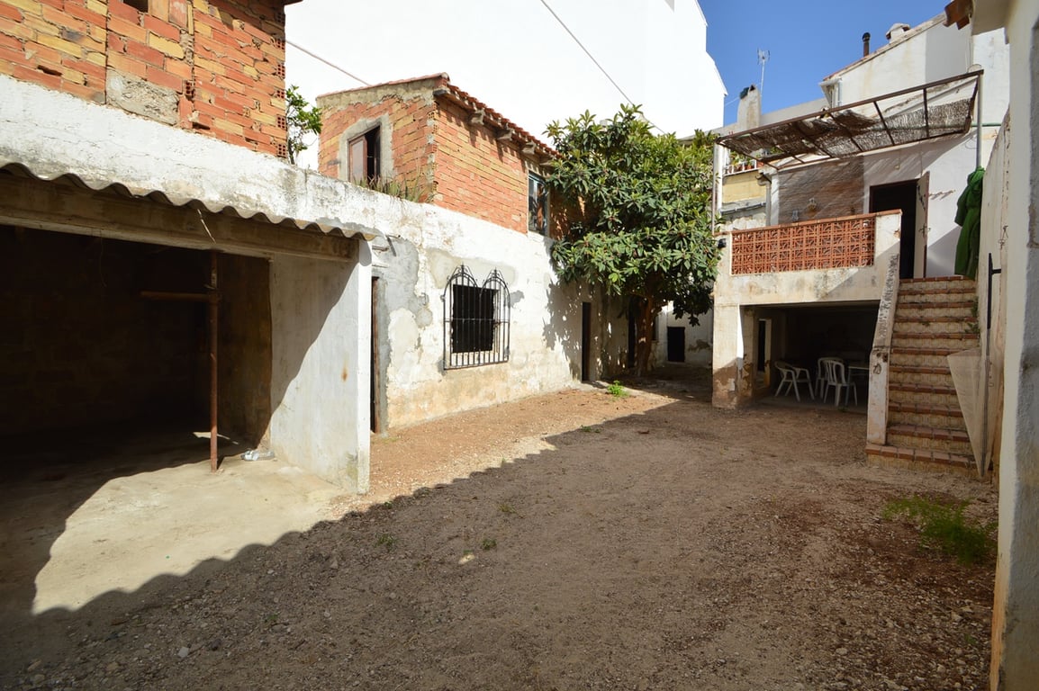Patio interior privado con suelo de tierra, dependencias anexas de ladrillo visto y una terraza elevada accesible mediante escaleras exteriores de obra.