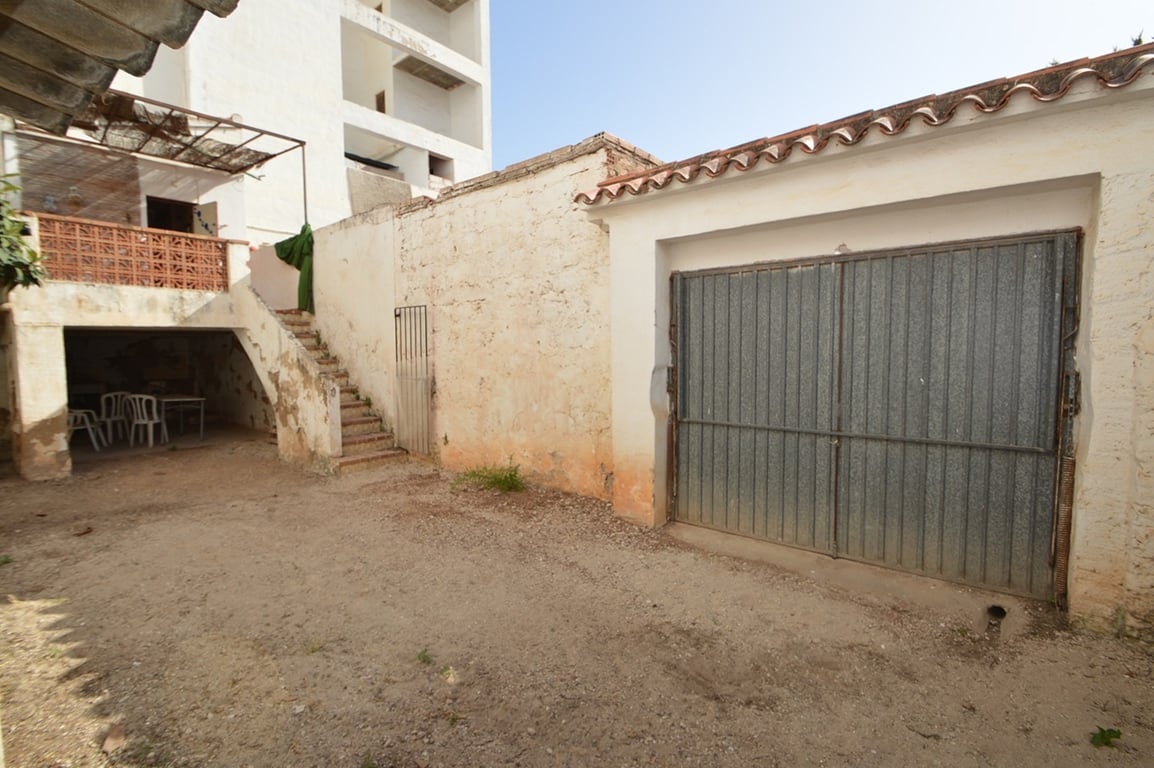 Patio trasero con portón metálico para aparcamiento privado, escalera exterior hacia la terraza superior y un porche cubierto ideal para almacenamiento.