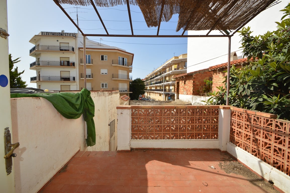 Terraza exterior con suelos de terracota y barandilla de celosía cerámica, bajo una pérgola metálica con cubierta de cañizo y vistas al entorno urbano.