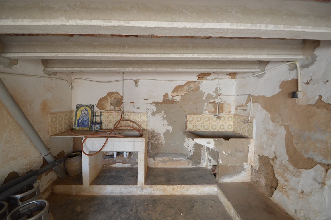 Zona de lavadero rústica con fregaderos de piedra originales, azulejos decorativos y vigas a la vista, ideal para un proyecto de restauración integral.