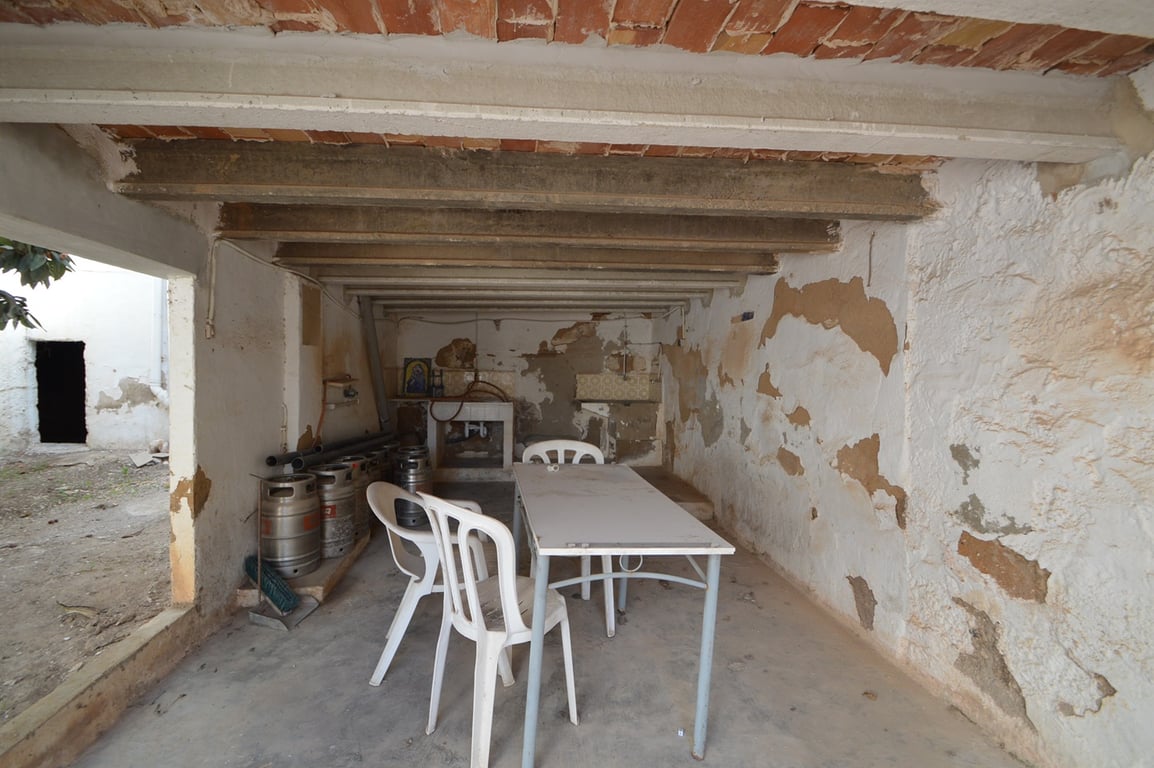 Zona de terraza cubierta con techos de vigas de hormigón y ladrillo visto, ideal para reformar como espacio de entretenimiento junto al patio.