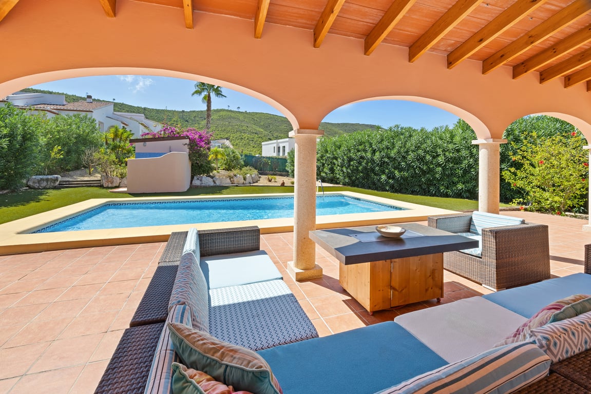 Amplia naya con vigas de madera y arcos de piedra que ofrece una zona de estar sombreada frente a la piscina privada y vistas a las montañas.