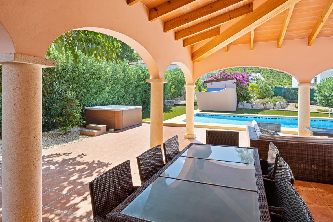 Amplia naya con vigas de madera y columnas de piedra, equipada con comedor exterior y vistas a la piscina, el jacuzzi y el entorno montañoso.