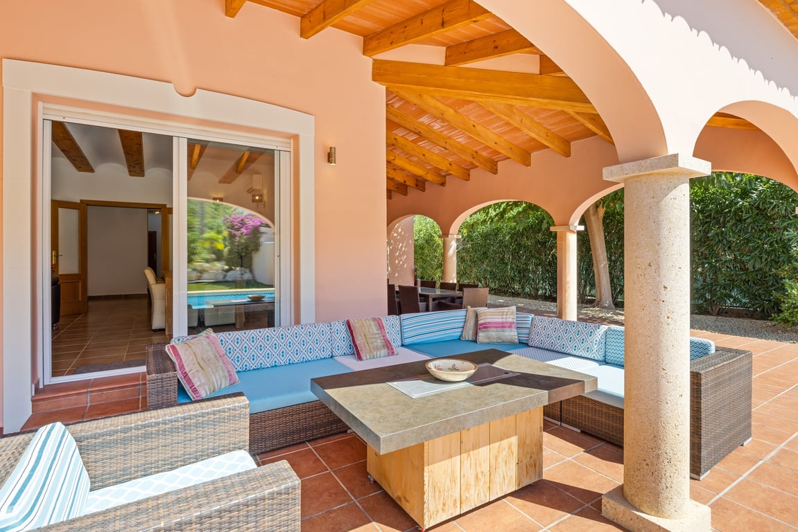 Amplia naya con vigas de madera y columnas de piedra Tosca, equipada con una zona de estar exterior y acceso directo al salón mediante puertas correderas.