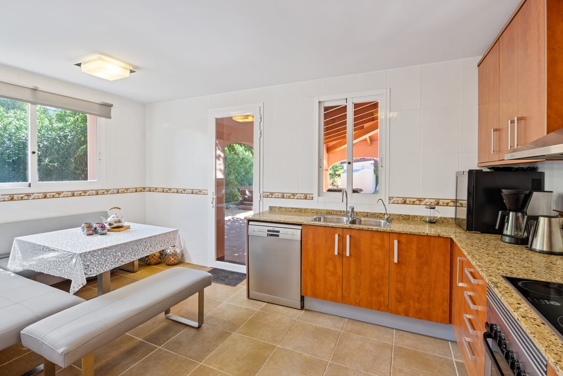 Cocina funcional en forma de L con encimeras de granito, armarios de madera y zona de desayuno integrada. Incluye acceso directo al exterior y abundante luz natural.