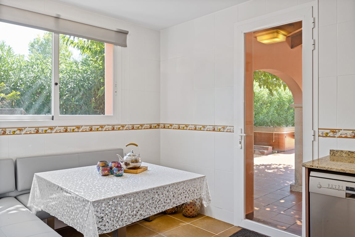 Luminoso rincón de desayuno en la cocina con banco esquinero y acceso directo a la terraza exterior a través de una puerta acristalada.